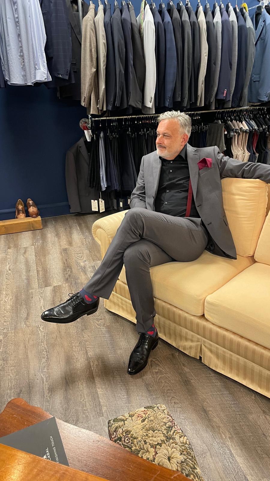 Ein älterer Herr im grauen Anzug sitzt entspannt lächelnd auf einem beigen Sofa