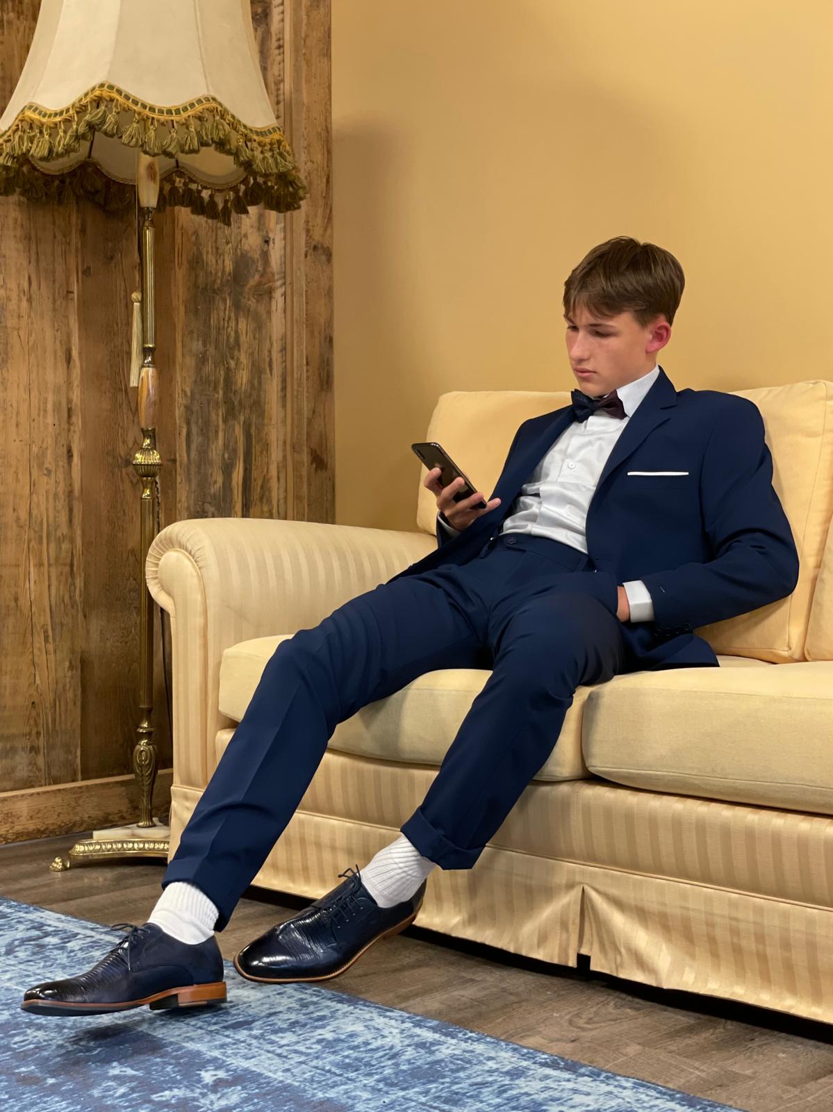 Junger Mann im blauen Anzug sitzt entspannt auf Sofa und blickt ernst auf sein Handy