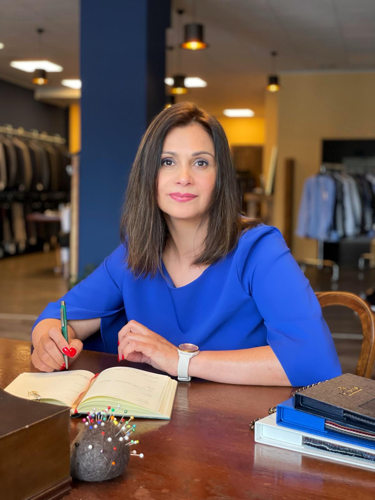 Eine Frau mit braunen Haaren und blauem Kleid lächelt leicht am Schreibtisch